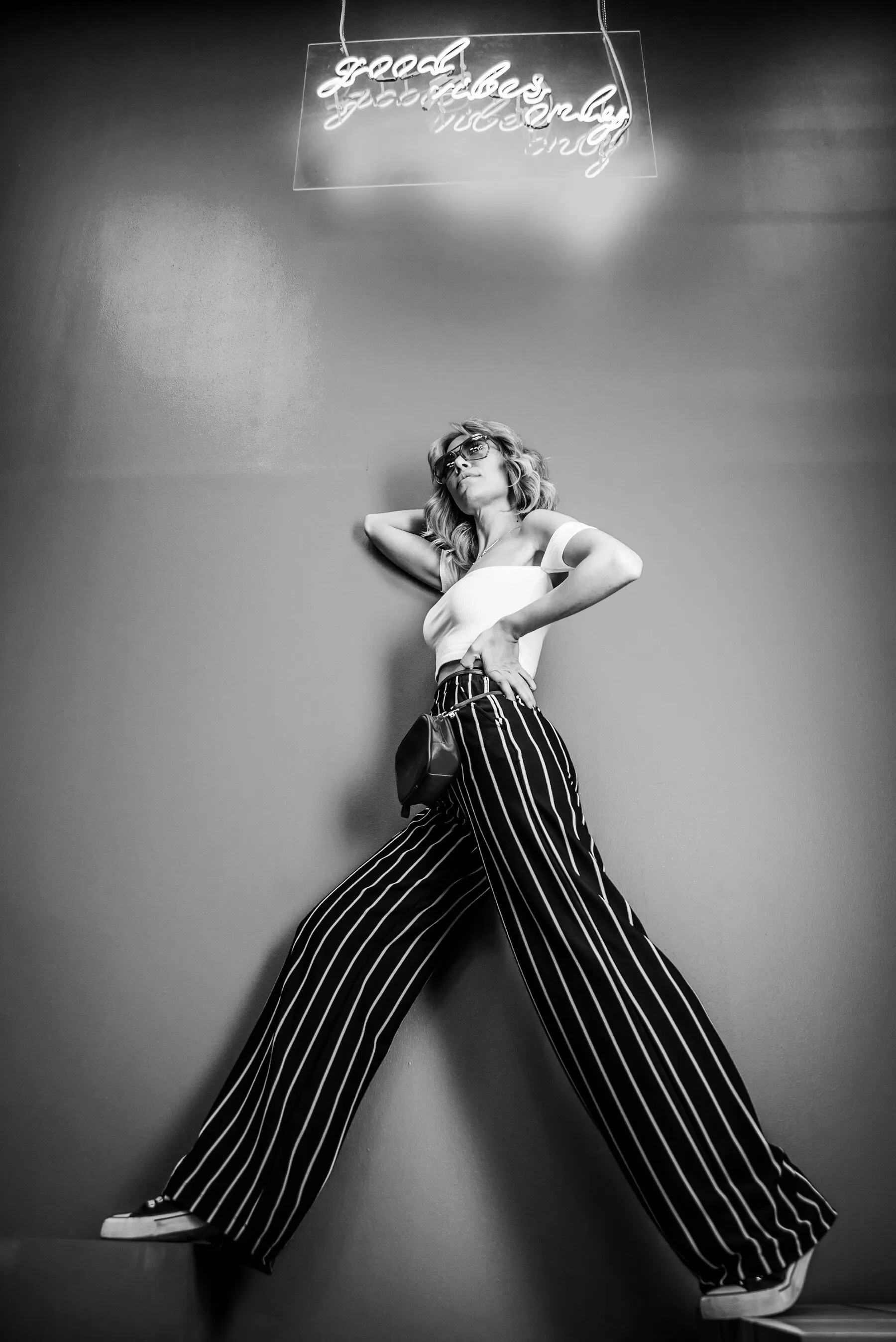 A figure in striped trousers posing under a neon sign
